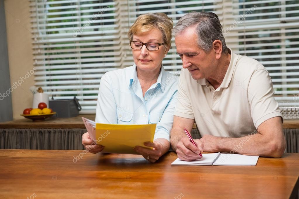 An older couple reviewing bills and notes while discussing expenses.